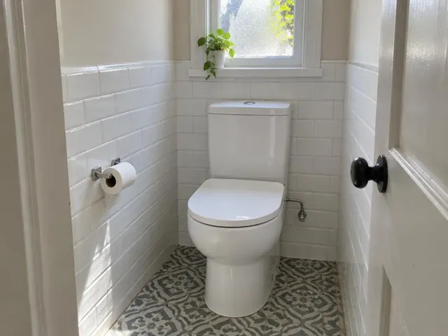 Clean white toilet in a tiled small bathroom with patterned floor and window light in Lewisham